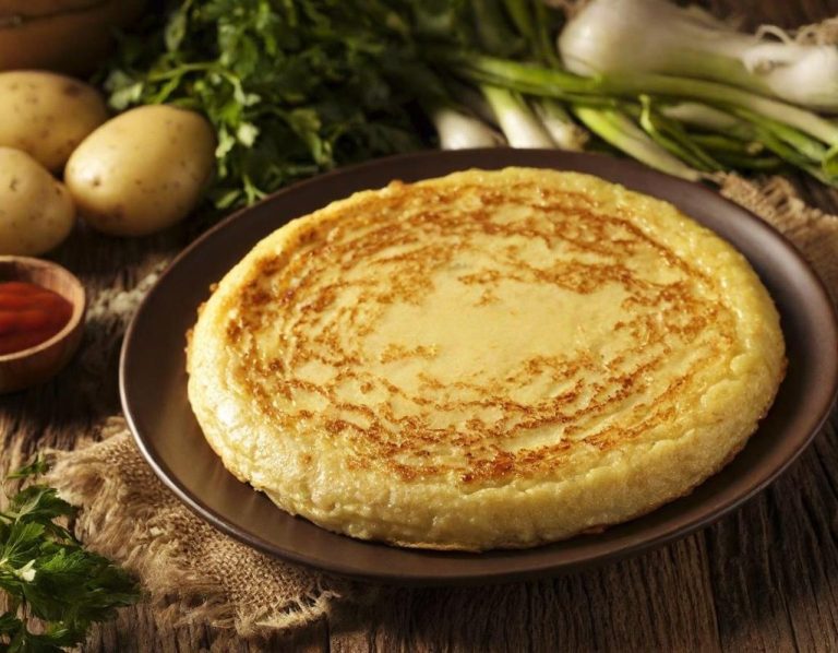 Tortilla de patata Tortilla española dorada, acompañada de patatas, cebollas y salsa roja en un plato.